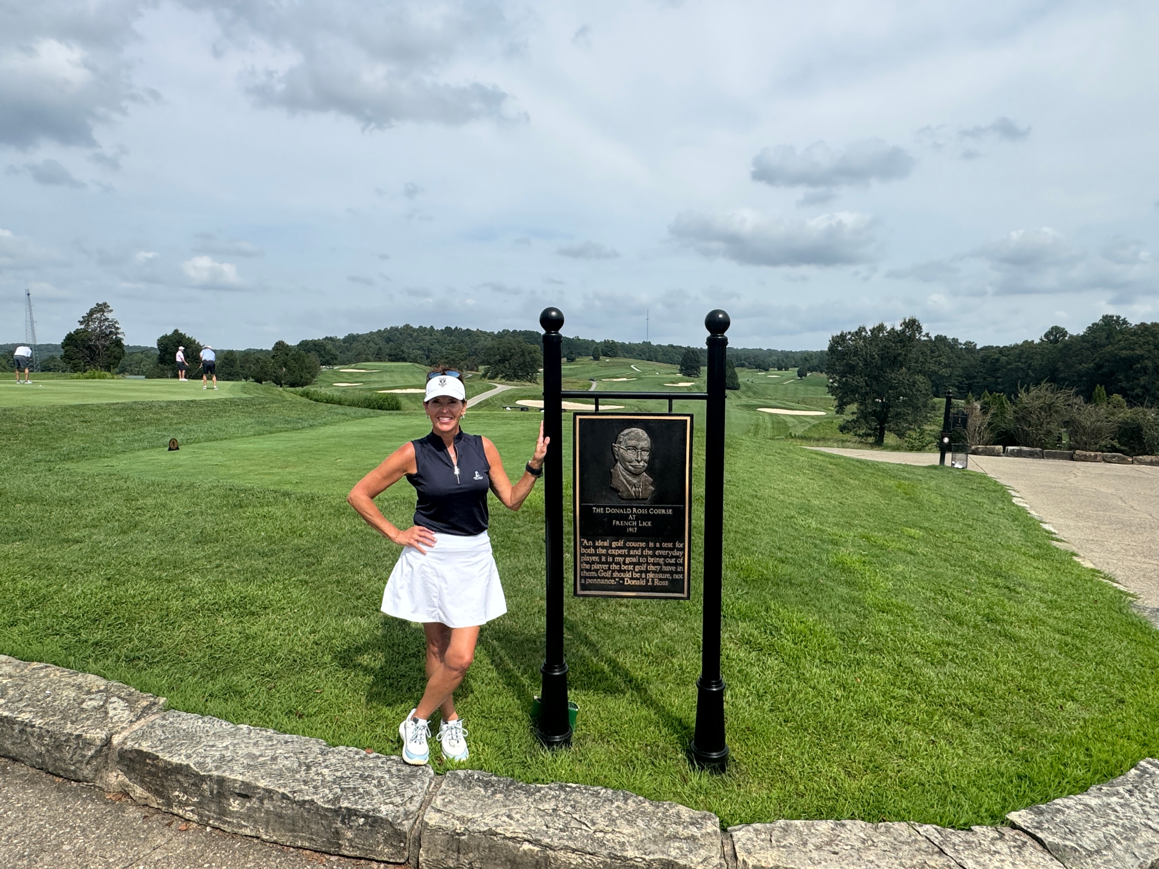Janet beside the Donald Ross plaque — the Indiana hills rolling out behind